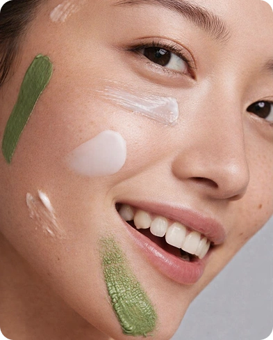 Close-up of a smiling woman with natural skin featuring green and white skincare product swatches